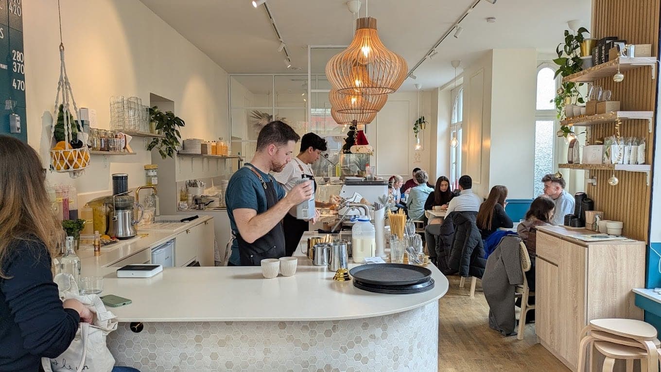A barista making coffee while people talk at the tables of Tulip Coffee in Bonn